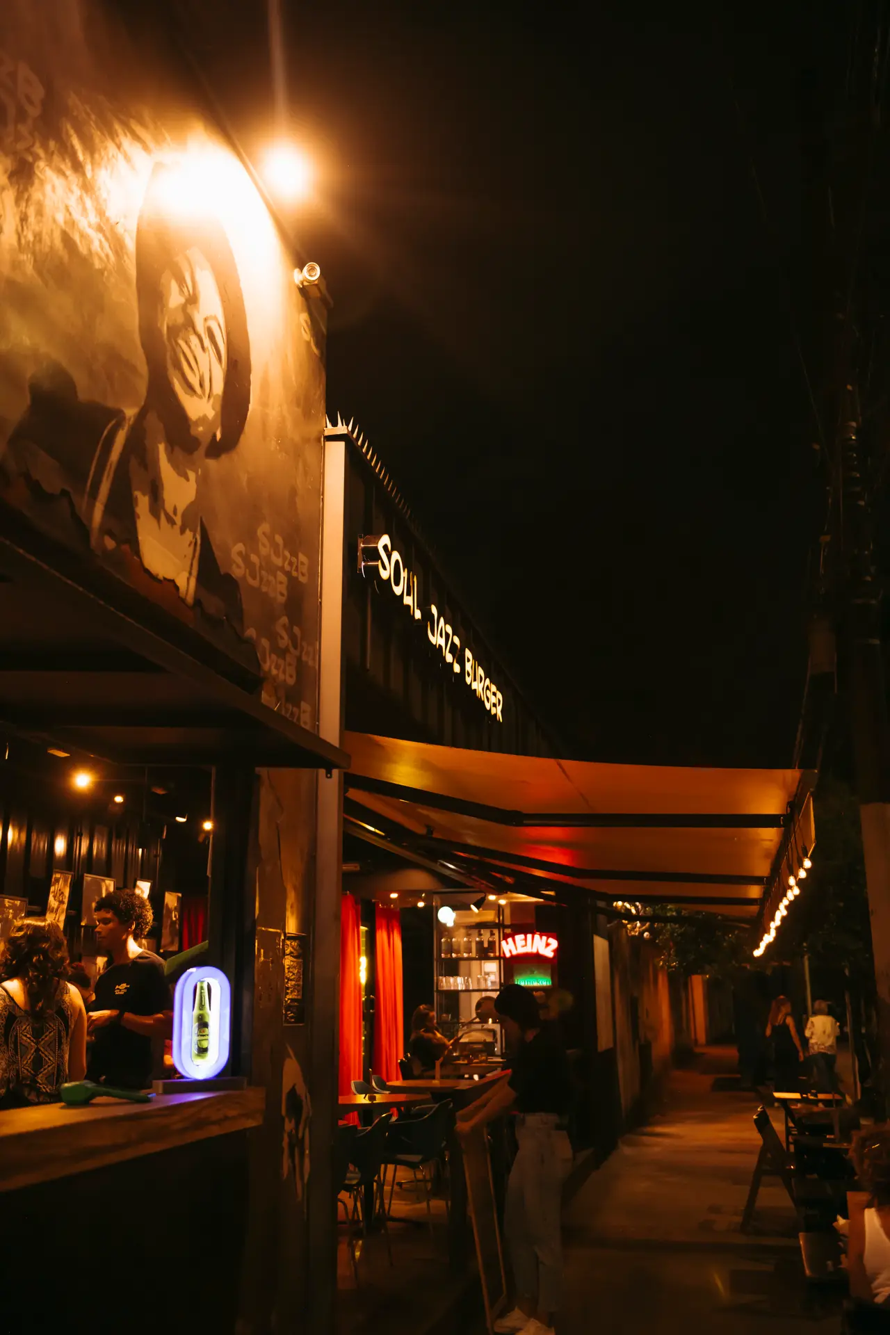 Calçada da Pampulha à noite, com o mural iluminado e o toldo de luzinhas